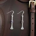 May include: A pair of silver-toned earrings with a unique design. Each earring features a long, slender bar with a small, rectangular purple bead in the center. The bottom of each earring has a textured, flared shape. The earrings hang from a simple hook.